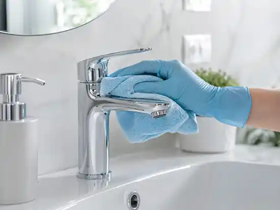 Cleaner using a soft cloth on bathroom taps to avoid surface damage.